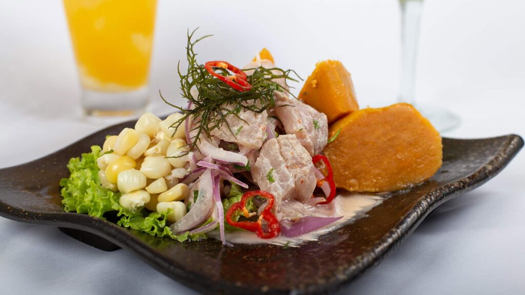 Delicious Peruvian ceviche on a dark plate with sweet potato, corn, and red onions.