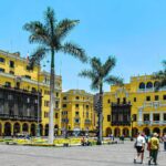 Plaza Mayor, Lima, Peru: A vibrant yellow colonial square under a bright blue sky, featuring palm trees, ornate architecture.